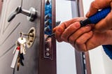 IMAGE: The hands of a locksmith working on a security lock with a screwdriver