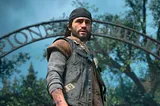 Sam Witwer as Deacon St. John in Sony’s PlayStation video game Days Gone. He’s  standing in front of a cemetary sign, wearing a jacket and a backwards hat.