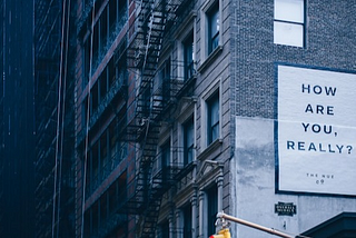 ‘How are you, really?’ poster on a side of a building. Photo by Des Récits on Unsplash