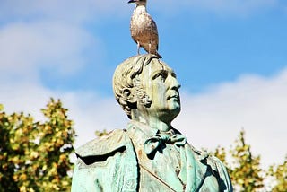 A statue of a prominent man,  with a live seagul on his head.