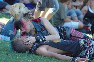 Two punks in love, on the grass in a crowd. Seemingly in a park