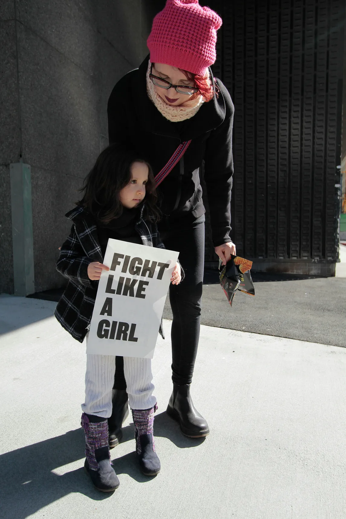 A woman with a little girl. The little girl is holding a sign that reads, Fight Like a Girl.