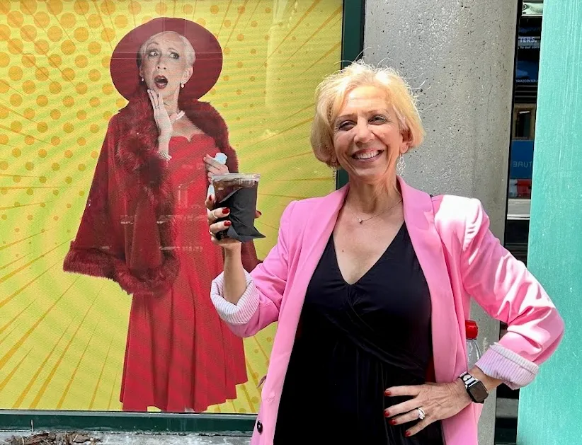 Actress Roz Potenza posing in front of poster for Sheer Madness.