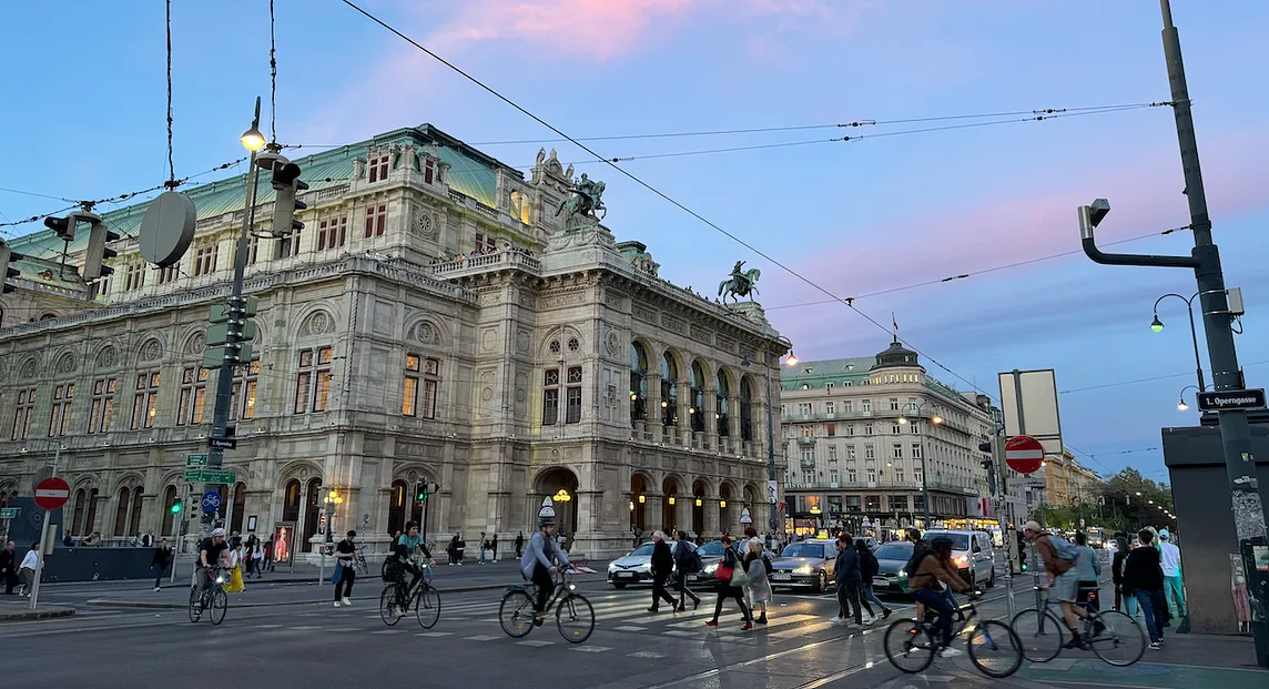 The Vienna State Opera building and its busy street, at dusk.