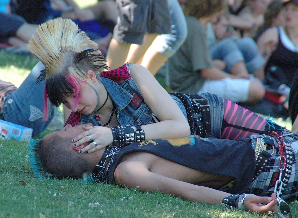 Two punks in love, on the grass in a crowd. Seemingly in a park