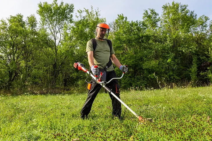 Man cutting grass in protective helmet and gloves