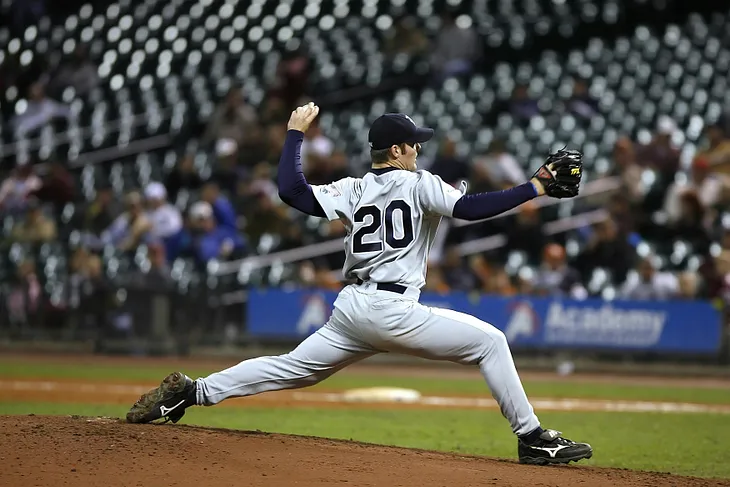 Baseball player pitching in front of stadium fans.