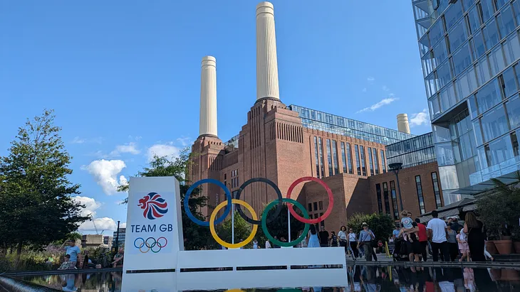 A large red brick structure with two cream chimneys in background and the Olympic rings in foreground