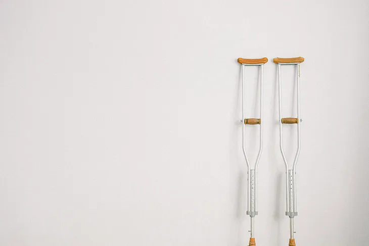 A pair of crutches rests upright on a white wall.