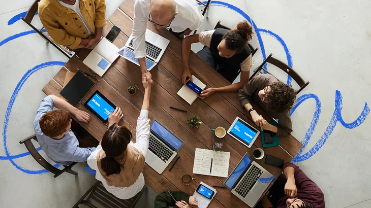 A meeting table seen from above with 8 people seated discussing ideas.