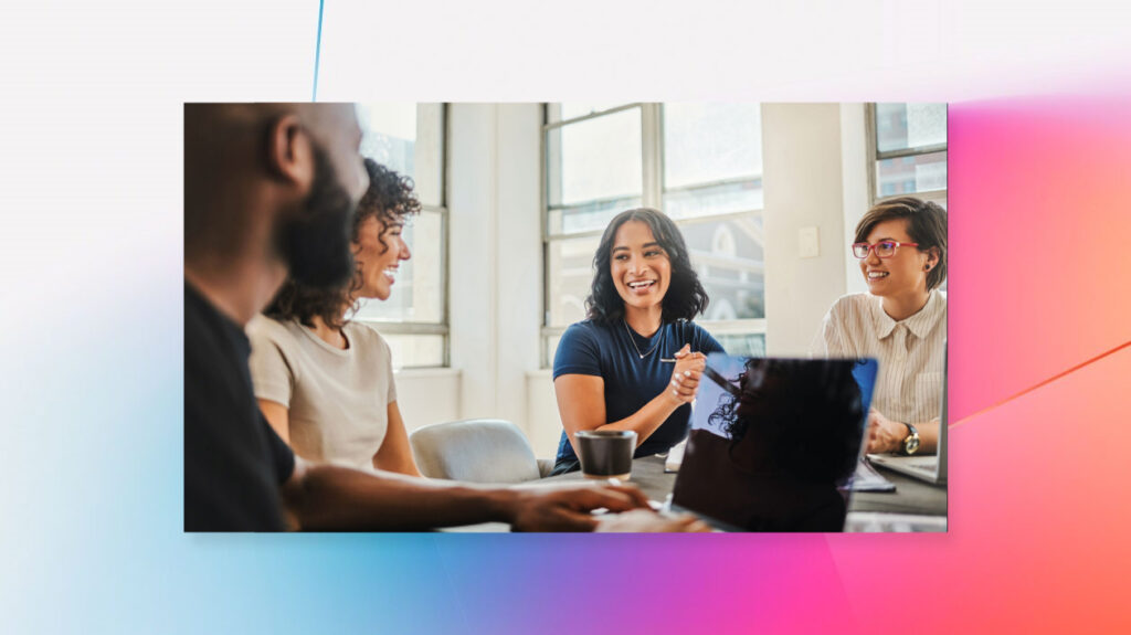 A diverse group of coworkers collaborate in an office space while one takes notes on his laptop.