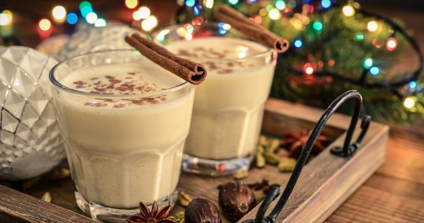 two glasses of two glasses of homemade eggnog recipe on a holiday themed wooden board