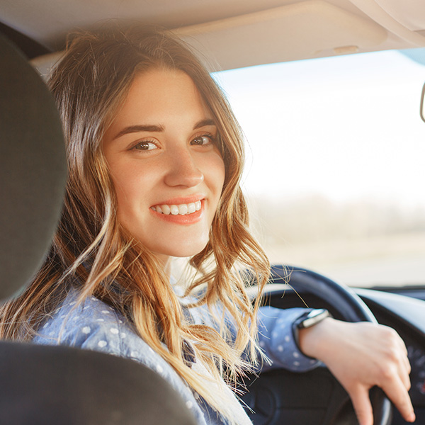 Close up portrait of pleasant looking female with glad positive expression, being satisfied with unforgettable journey by car, sits on driver`s seat, enjoys music. People, driving, transport concept