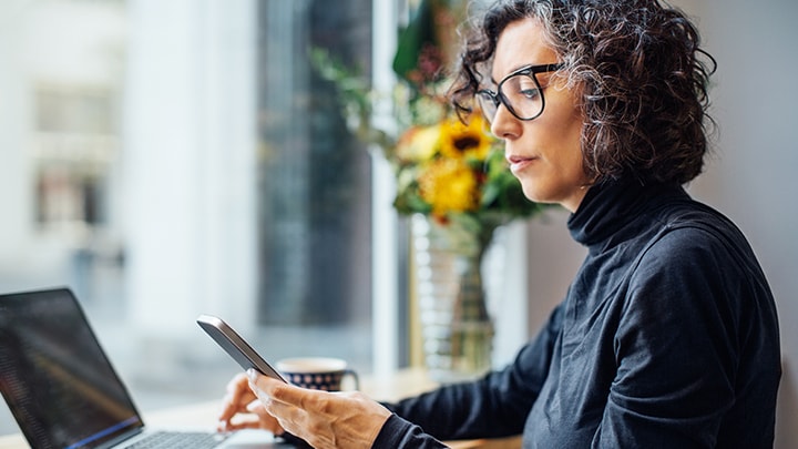 A person looking at a cell phone while working on laptop