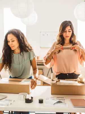 Two busy businesswomen packaging items and checking orders, illustrating a business that's growing with PayPal