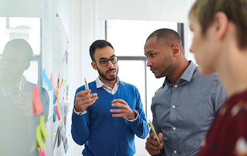 three people having a meeting in front of a whiteboard