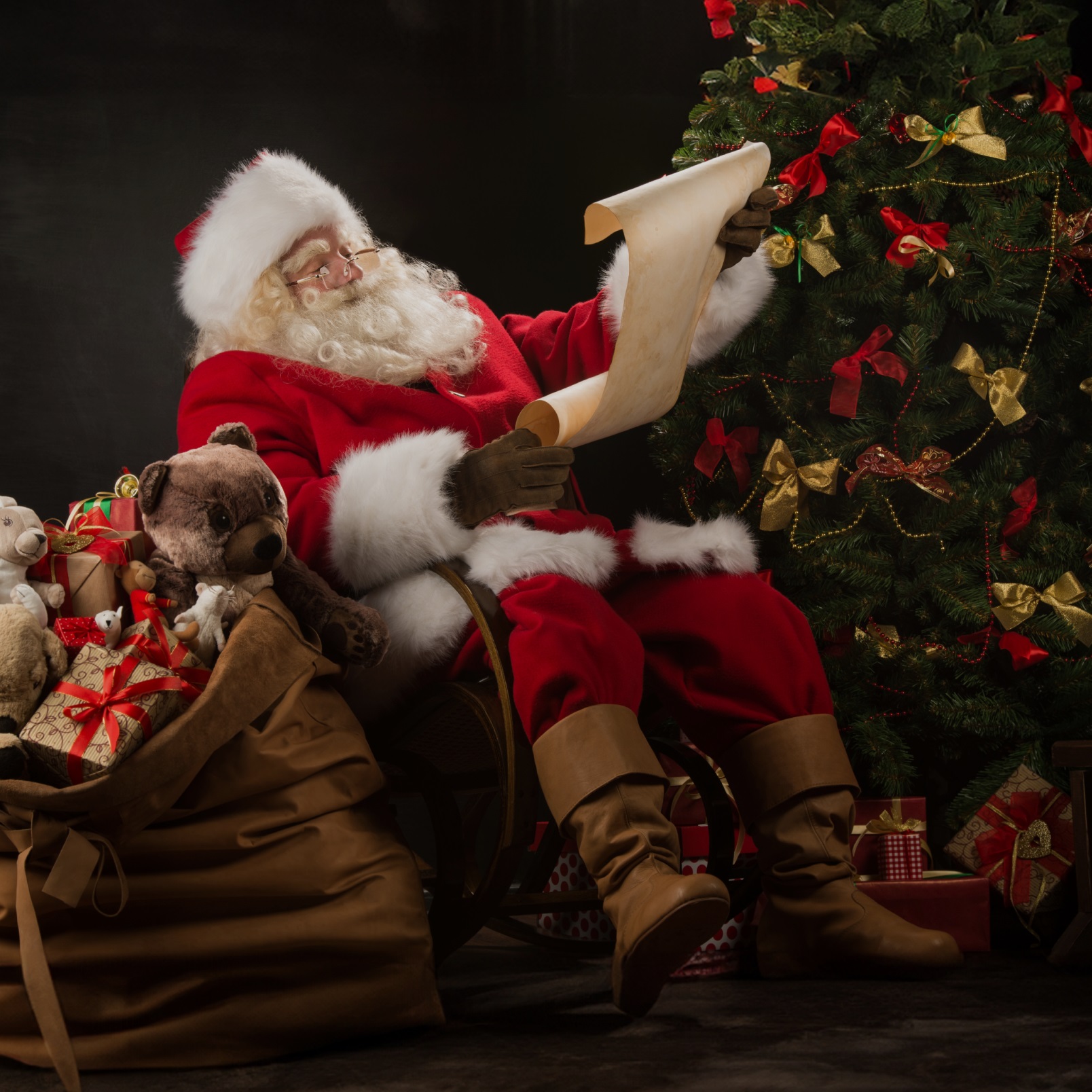 a picture of santa next to a christmas tree reading a list