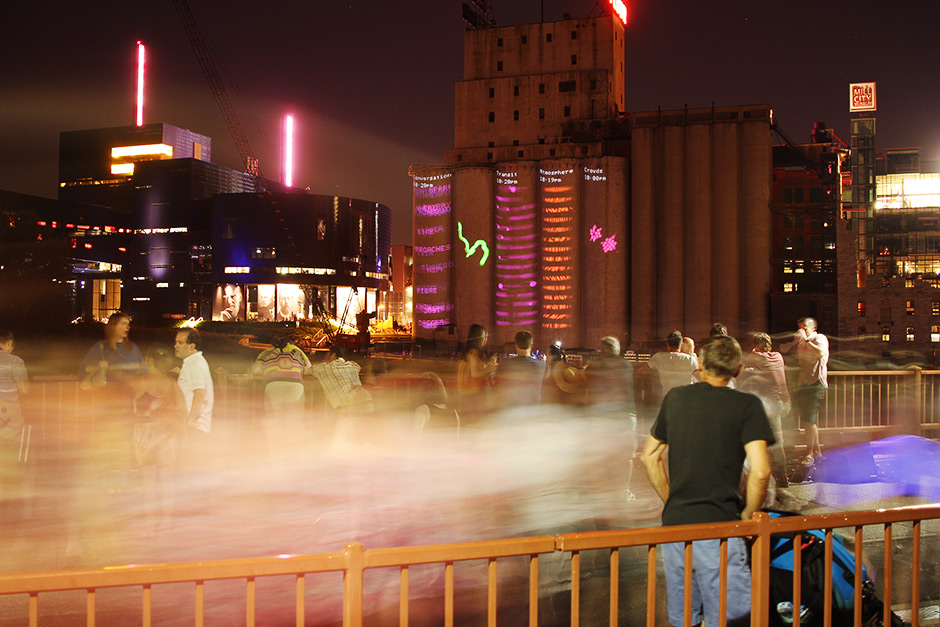 people on a bridge watching visualizations projected on silos