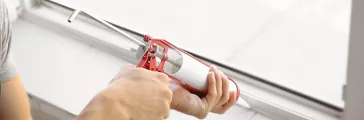 Man squeezing caulk onto window seal.