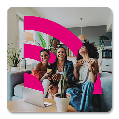 Three women smiling on a couch with a laptop open in front of them.