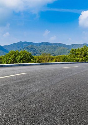 An empty highway skirting green hills.