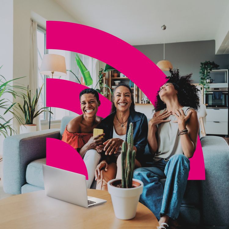 Three women smiling on a couch with a laptop open in front of them.