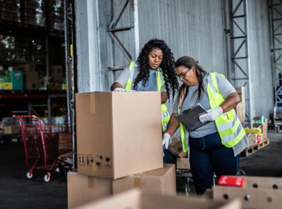 Two employees in yellow caution vests checking boxes in a shipping area.