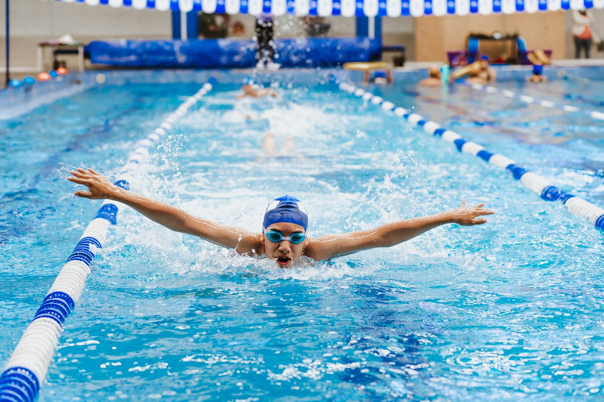 A person wearing goggles and a cap swims in a pool.