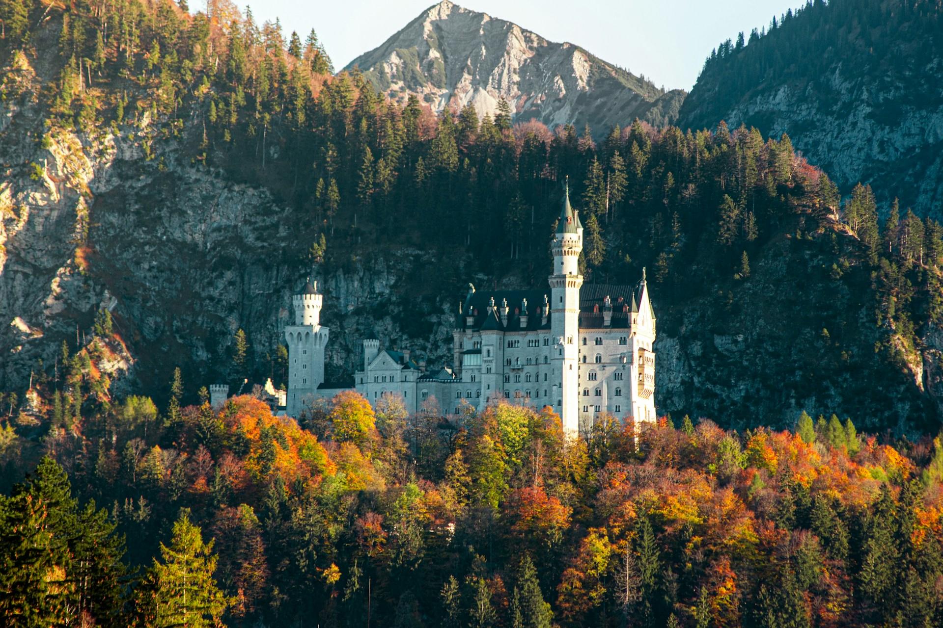 White castle surrounded by trees and mountains.