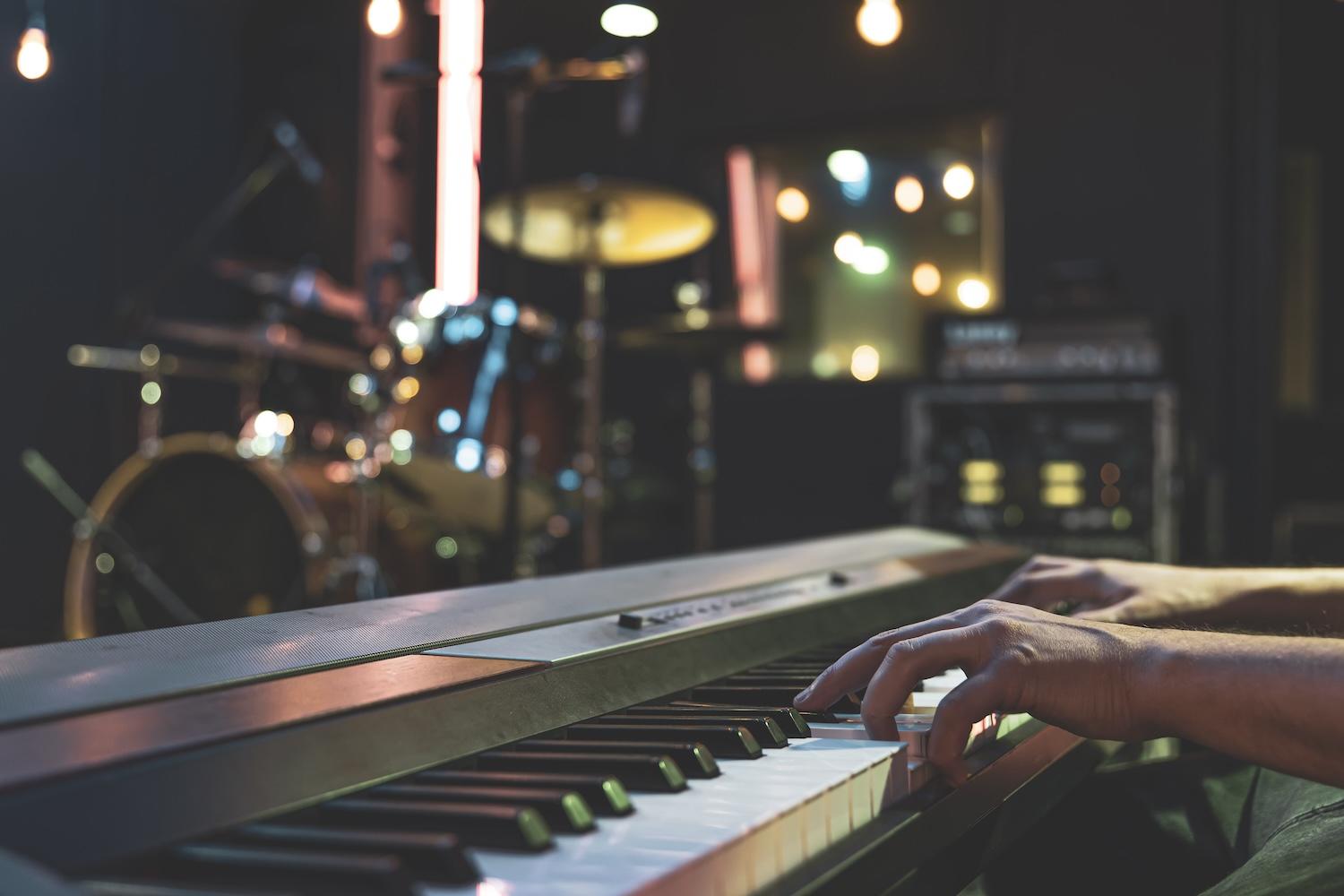 Gros plan sur les touches d'un piano avec les mains d'un pianiste, arrière-plan flou sur d'autres instruments.