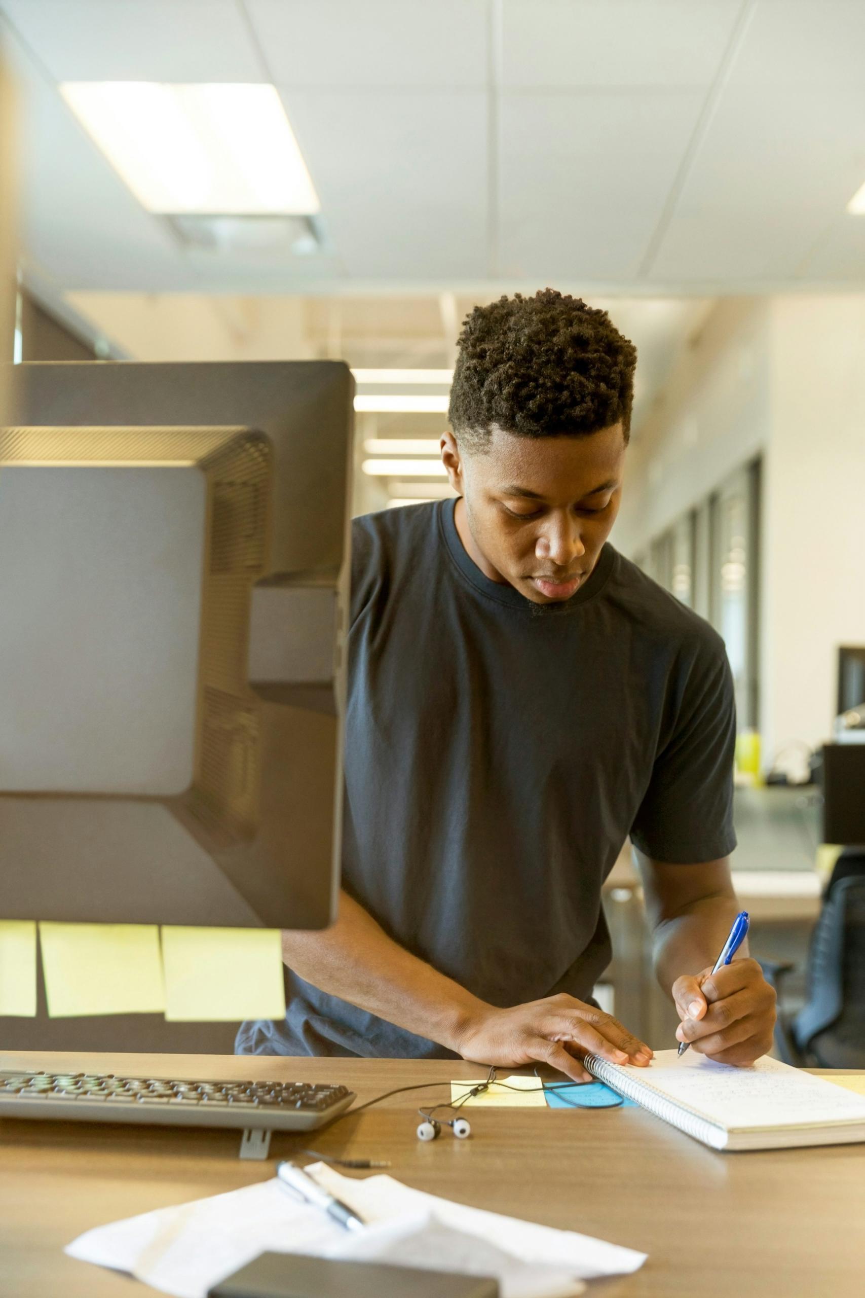 Personne en train de travailler sur son carnet devant un ordinateur de bureau 