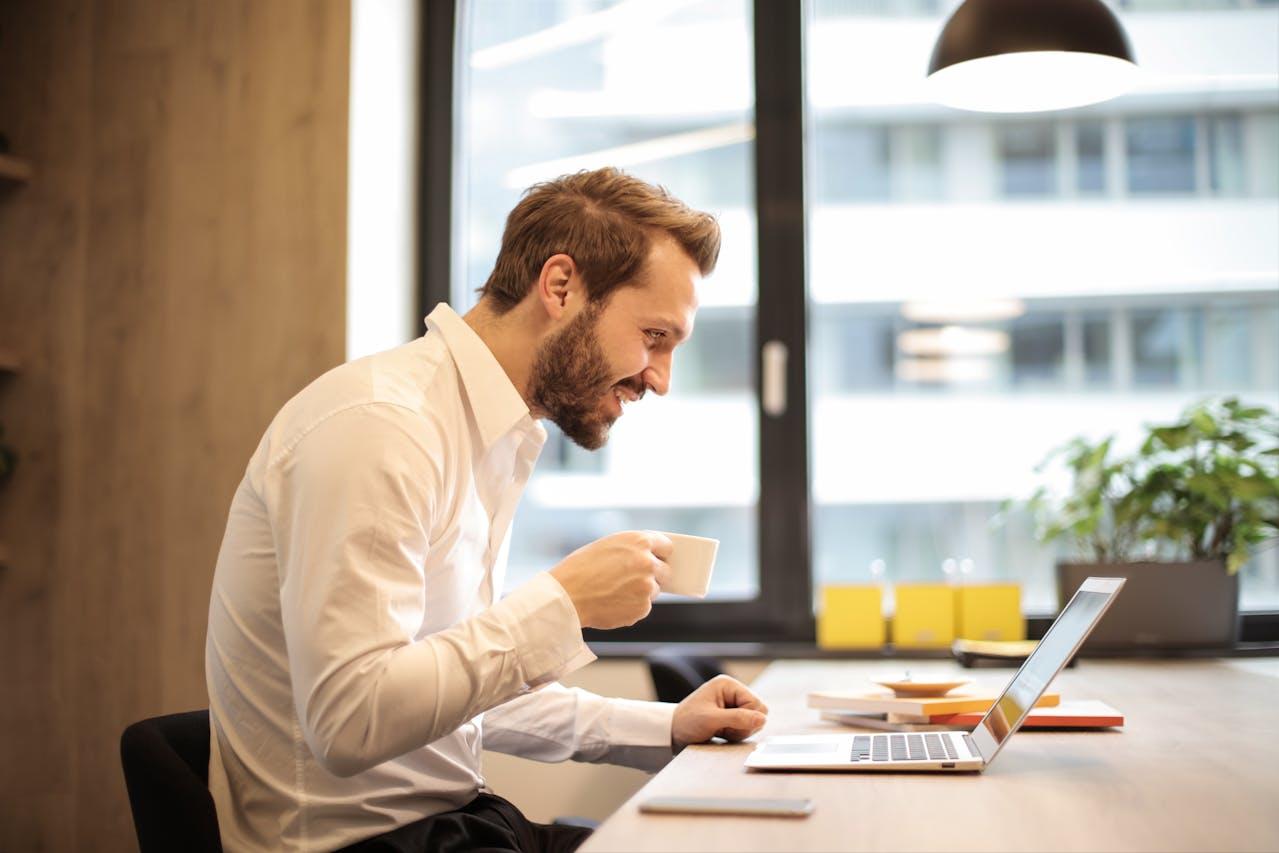 Homme assis dans un café, un café à la main, devant son ordinateur en train de suivre une formation Excel.