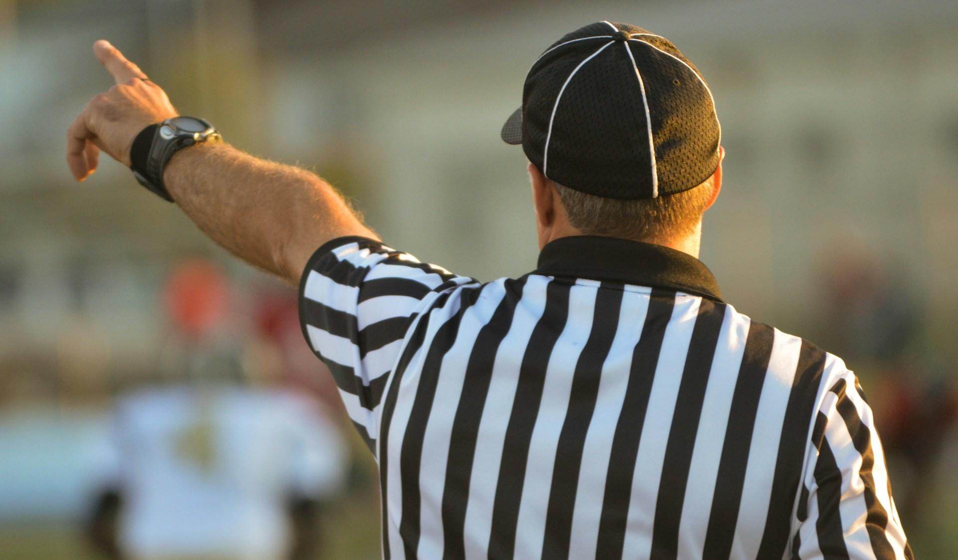 A man in a referee uniform gives a sign by pointing.