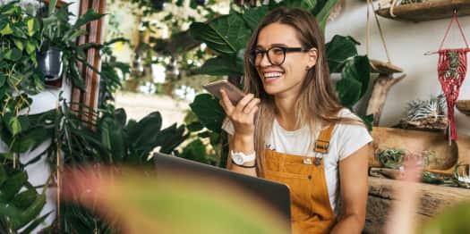 Trabajadora de una tienda de plantas sonríe sentada mientras habla por teléfono móvil.