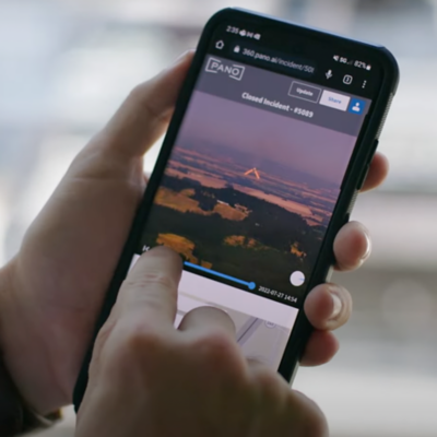 La mano de una persona sosteniendo un smartphone mientras la otra mano toca un video de un paisaje.