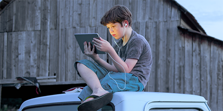 Boy sitting on top of truck looking at screen