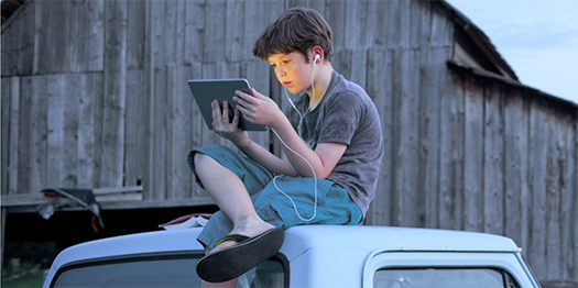 Boy sitting on top of truck looking at screen