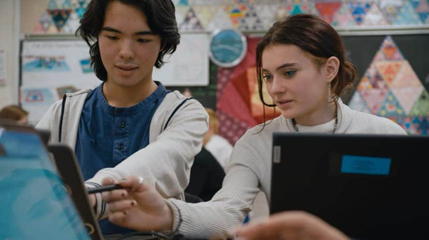 Two high school aged students, each with their own laptop, collaborate on an assignment in class.