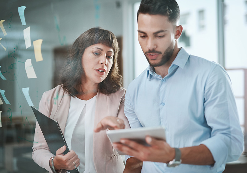 two employees in office attire looking at a tablet