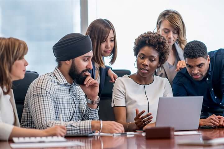 diverse group of employees huddled over a laptop on a conference table