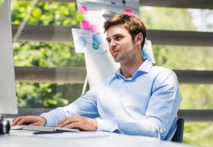 male employee sitting in front of a computer in a sunlit room