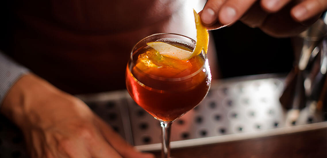 close up of drink with orange peel being placed into it