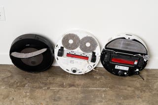 Three robot vacuums propped up on a wall, exposing their undersides.