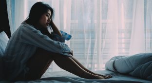 Unhappy beautiful Asian woman sitting on a bed looking sad and lonely