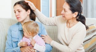 Mature woman comforting adult daughter with baby in living room at home