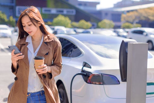 Person looking at their phone while charging an electric vehicle