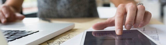 Close up of female architect at laptop using digital tablet in office