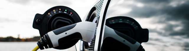 Black electric car overlooking coastal waterway while charging on a cloudy day