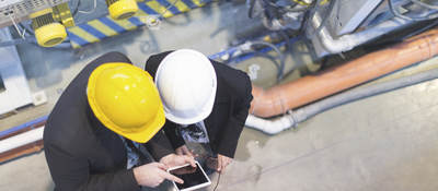 Two men in hard hats on a factory floor consulting over a tablet.