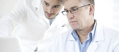 Two men in lab coats looking at a laptop. 